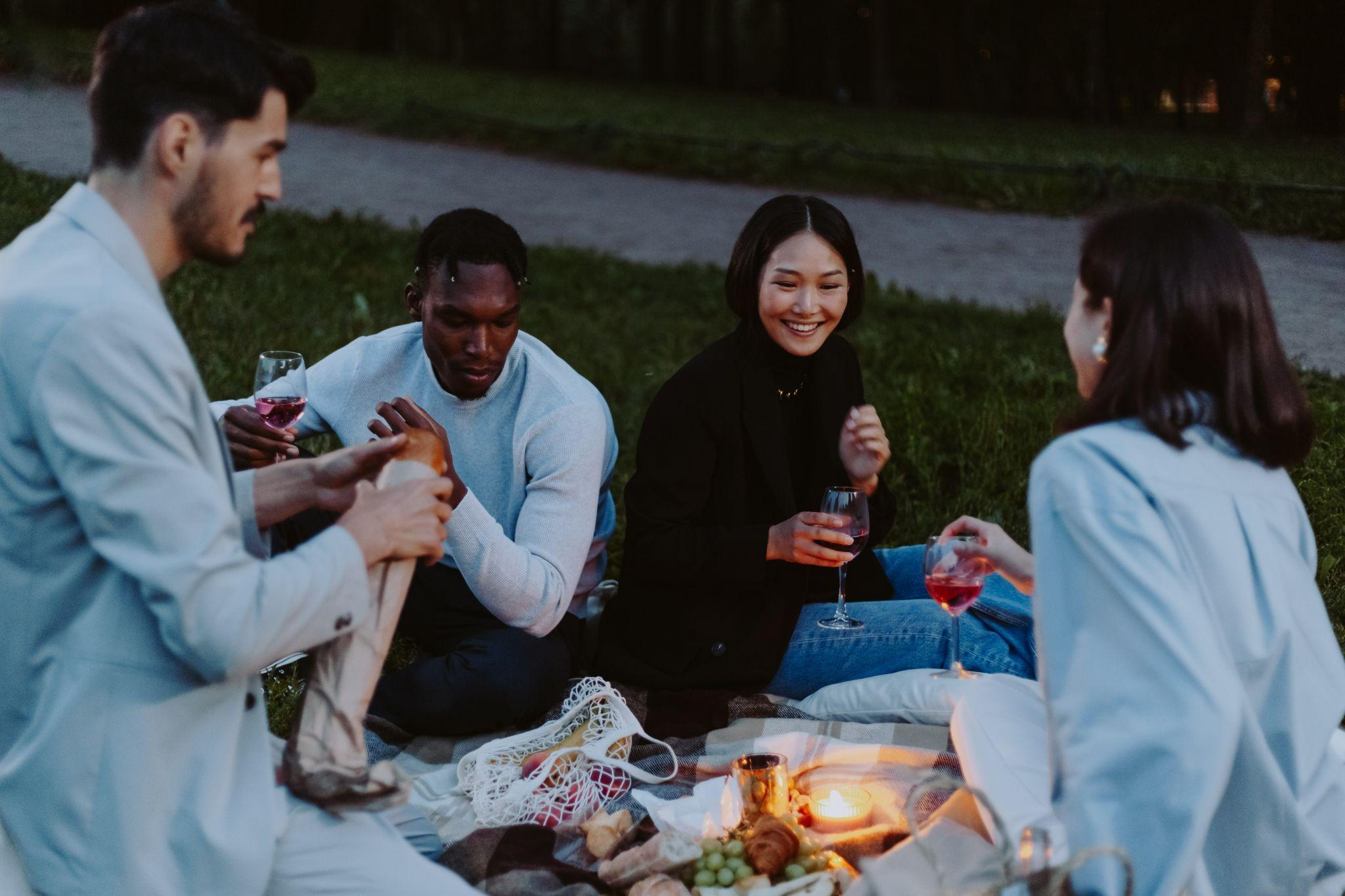 A group of friends sitting on a picnic blanket while having Cconversation