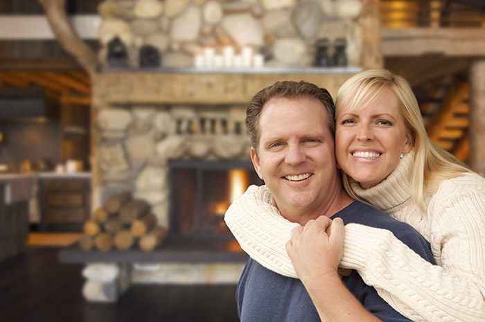 Happy Affectionate Couple at Rustic Fireplace in Log Cabin.