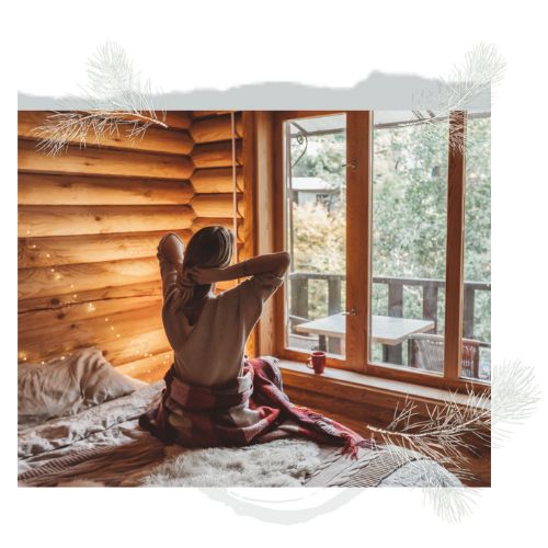 woman in log cabin home looking out at scenery from bedroom